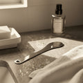 A stainless steel fragrance tool on a luxury marble bathroom counter, providing a solution to prevent perfume oil stains on delicate clothes.